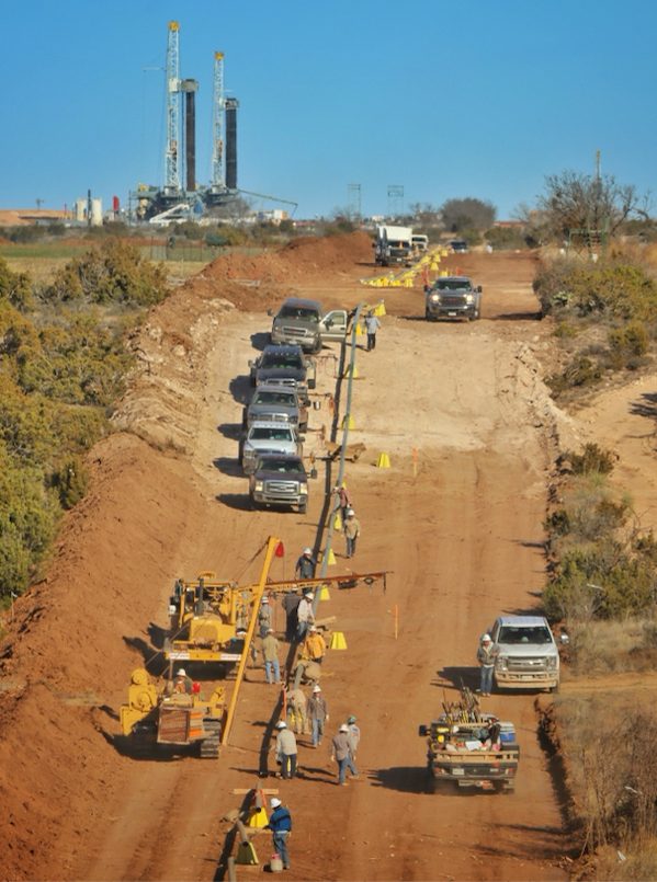 KES crew performing pipeline work with drilling rigs visible in the background