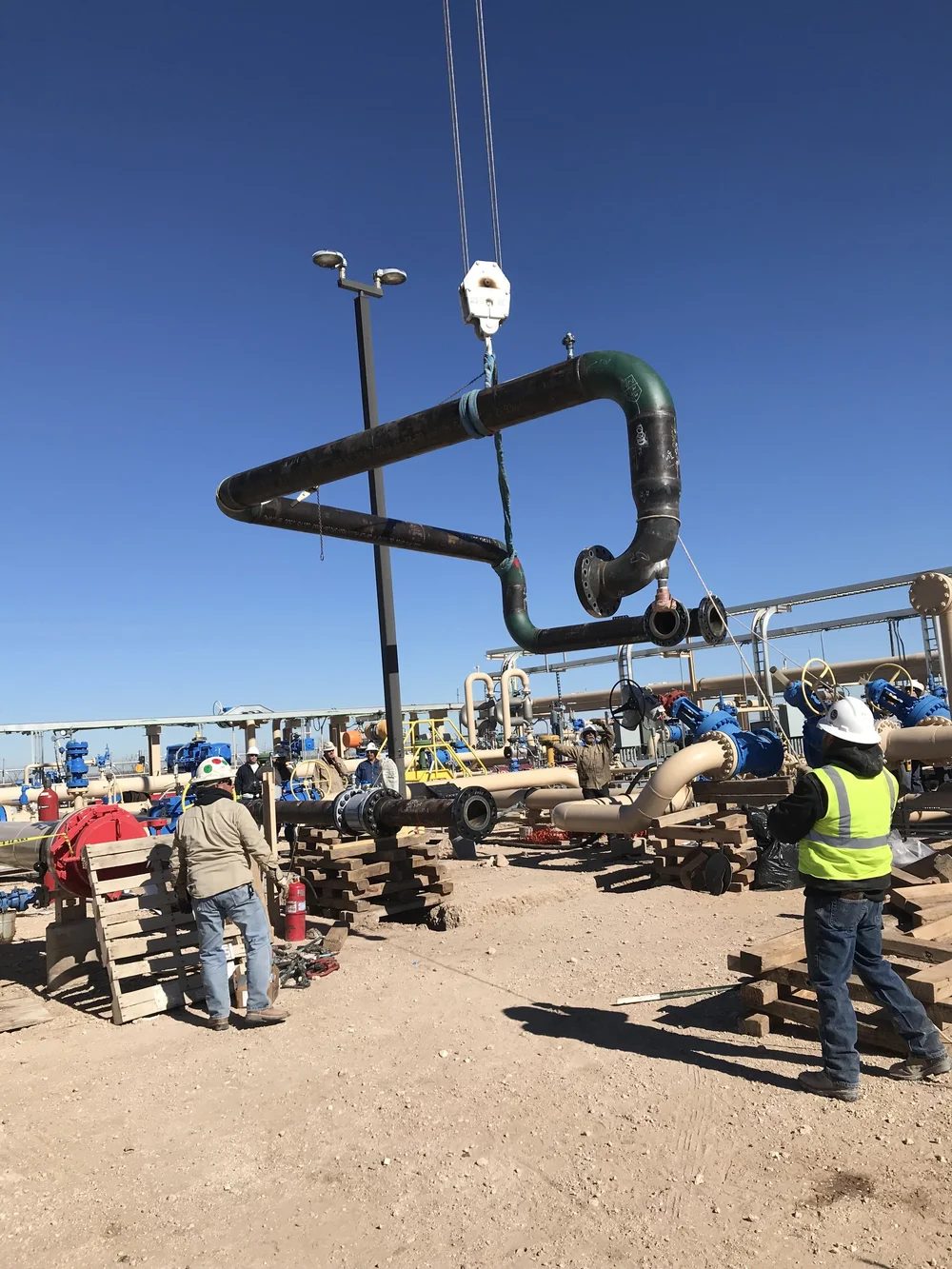 Crew rigging facility piping into place with a crane