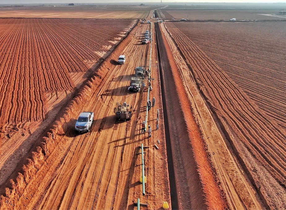 Aerial view of pipeline trench crew and equipment lined up across farmland
